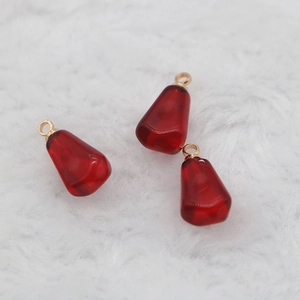 Deep red pomegranate seed resin charms with gold rings on white faux fur background