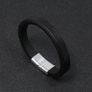 Detailed view of black leather bracelet with silver rectangular magnetic clasp on textured background