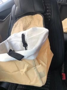 Close-up of the beige fabric pet car seat bag with black nylon straps on a leather seat