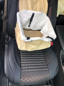 Close-up of beige car pet booster seat with breathable fabric on black leather car seat