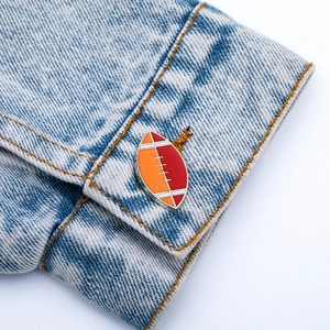 Vue macro d'un pin's de rugby émaillé orange et rouge sur la manche d'une veste en jean