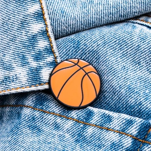 Détail macro d'un pin's basket-ball orange attaché sur une poche en jean bleu coton