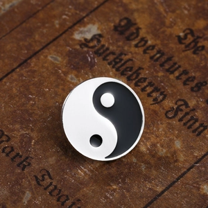 Makroaufnahme der Yin-Yang-Emaille-Anstecknadel auf antikem Buch mit Metalldetails