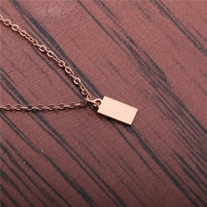 Polished rose gold rectangular bar pendant necklace on a minimalist wood grain background