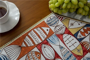 Macro view of chenille table runner featuring colorful fish patterns on dark wood
