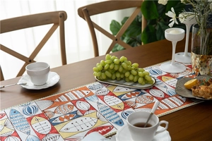 Detailed chenille table runner with colorful fish pattern on a rustic wooden dining table