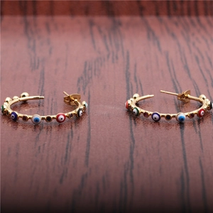 Detailed view of gold hoop earrings featuring colorful evil eye beads on wood background