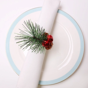 Detail of Christmas napkin ring with pine cones, red bells and green pine needles on white napkin