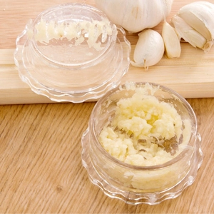 Macro shot of transparent plastic garlic grinder with minced cloves on wooden board