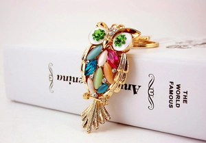 Detailed view of a golden owl keychain featuring colorful oval gemstones and textured wings