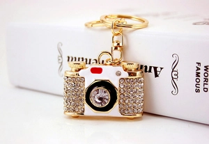 Macro detail of gold camera keychain with sparkling rhinestones and crystal lens