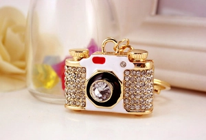 Close-up of a crystal-encrusted camera keychain with white enamel and golden metal finish