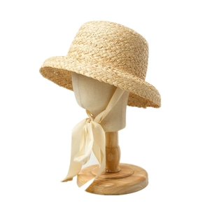 Detailed view of hand-woven raffia sun hat with silky ribbons on wooden stand