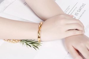 Close-up of a polished golden twisted cuff bracelet worn on a wrist over a white background