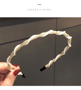 Detail view of woven metal and pearl headband held by hand against a grey wall
