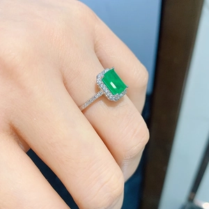 Macro shot of emerald cut green gemstone ring with white diamond pave on fingers