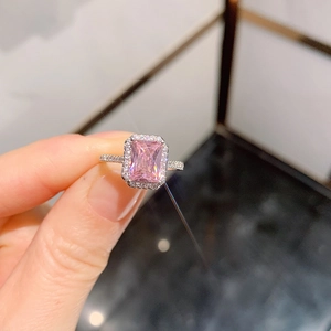 Macro view of a rectangular pink halo engagement ring with pavé diamond band on fingers
