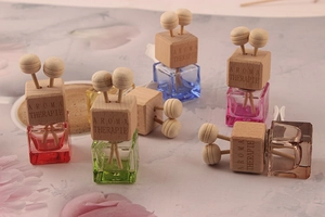 Colorful square glass car perfume bottles with wooden caps and diffuser sticks on floral background