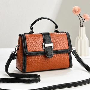 Caramel woven texture handbag with black straps and silver buckle in a minimalist setting
