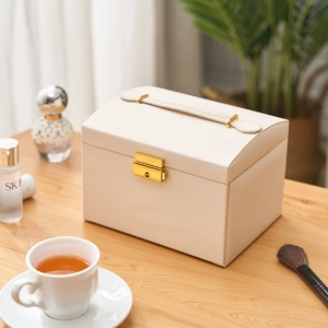 Three-layer beige leather jewelry storage box with gold lock and handle on a desk