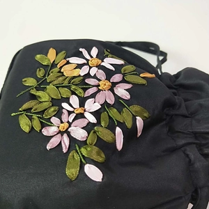 Detailed macro view of 3D silk ribbon floral embroidery on black satin drawstring bag