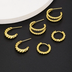 Three pairs of golden C-shaped twisted rope hoop earrings on a black textured background