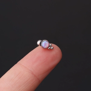 Macro shot of a mini silver cartilage stud with a pink opal stone on a fingertip