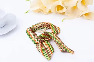 Close-up of golden watch with green and orange striped silk ribbon strap on a desk