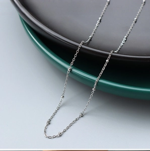 Detail of 1.2mm steel bead cross chain necklace on a minimalist ceramic plate