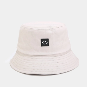 Detailed view of cream canvas bucket hat featuring a black square smiley face patch