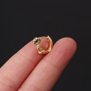 Golden snake-shaped ear cuff with green gemstone eyes held between fingers