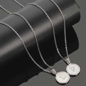 Detalle del collar de acero plateado con colgantes L y V sobre incrustación de nácar