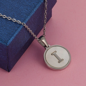Collar de acero plateado con colgante redondo de nácar y letra I sobre fondo rosa