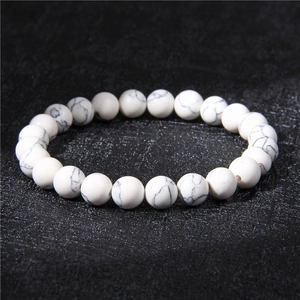 Macro detail of 8mm white howlite stone beads on a black textured background