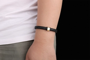 Détail d'un bracelet en cuir tressé noir au poignet avec fermoir en acier doré poli