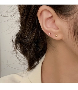 Close-up of minimalist gold ball and square zircon stud earrings set on a female ear