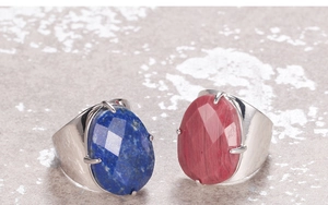 Detail of wide metal rings featuring oval lapis lazuli and pink stone in four-prong settings