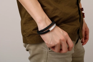 Detail of men's double-layered braided black leather bracelet with brushed metal plate