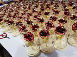 Macro detail of red foil roses in glass domes with gold stems on wooden bases