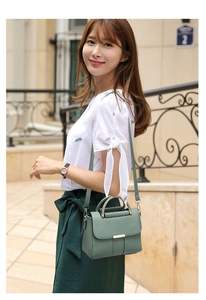 Deep green faux leather handbag with metal buckle worn by model in outdoor street setting