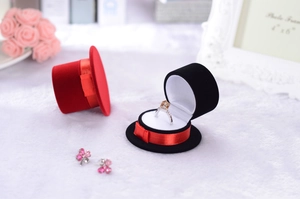 Velvet top hat jewelry boxes with a ring and pink flower earrings on a plush surface