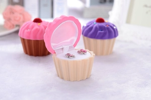 Macro shot of cupcake-shaped velvet jewelry boxes with pink floral earrings inside