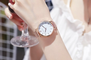 Gros plan d'une montre en maille milanaise or rose au poignet tenant un verre de vin
