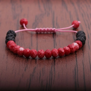 Lava stone and red faceted bead braided bracelet on a dark rustic wood surface