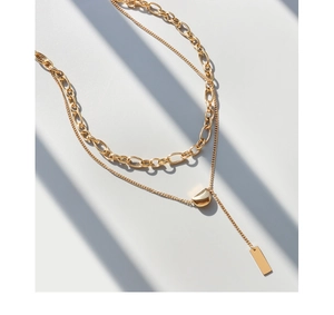 Detail of layered gold titanium necklace with geometric pendant and rectangular tassel