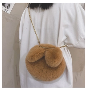 Brown fluffy round plush bag with rabbit ears and golden chain strap shown on a model