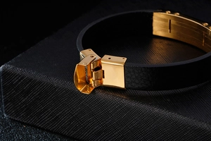 Dettaglio macro della chiusura dorata in acciaio inox su bracciale in pelle nera intrecciata