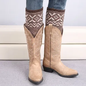 Bohemian knit leg warmers with geometric diamond patterns worn over denim jeans and western boots