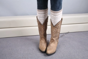 Détail de jambières en tricot avec motifs bohèmes dans des bottes de cowboy marron