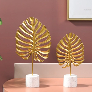 Set of two gold metal monstera leaf ornaments on white marble bases for home decor